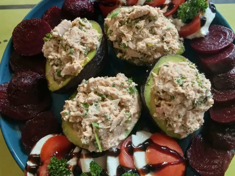 Aguacates rellenos de atún y hierbas rodeados de tomate con mozzarella y balsámico y rodajas de remolacha en una fuente azul
