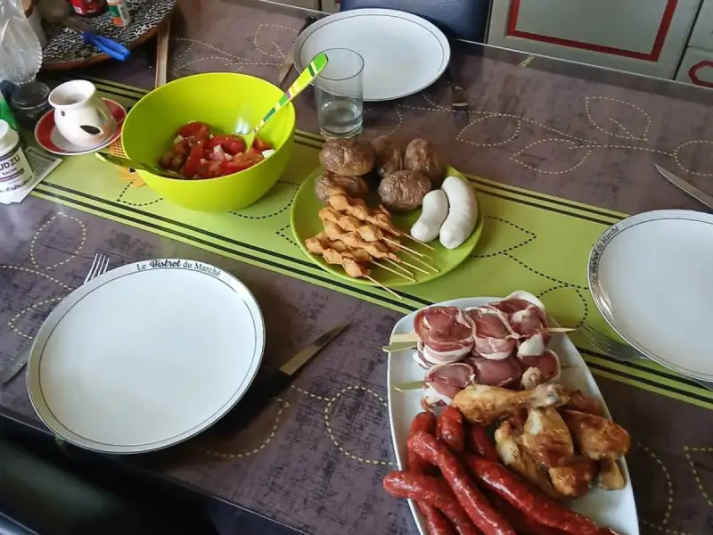 Brochettes de poulet crues sur une table de barbecue avec saucisses, pilons, roulades au lard et salade de tomates