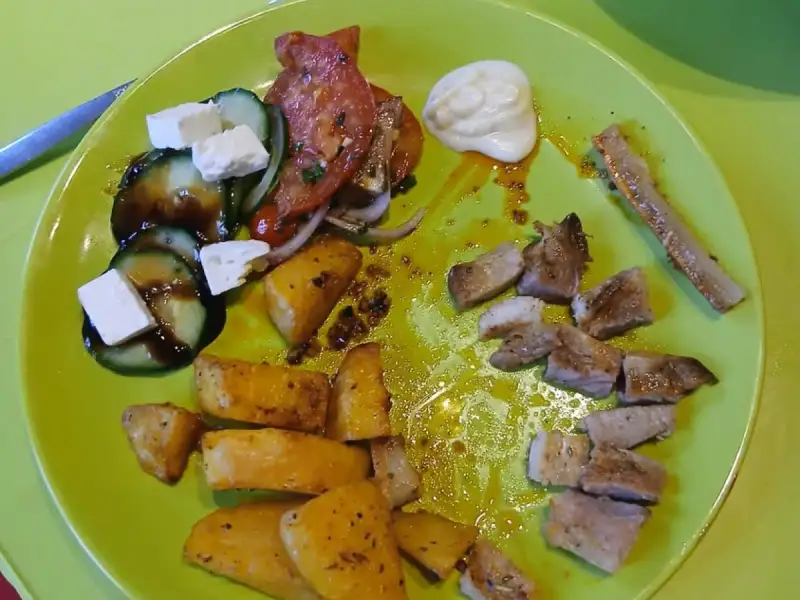Assiette de côtes de porc grillées en morceaux, pommes de terre rôties et salade grecque concombre, tomates et feta
