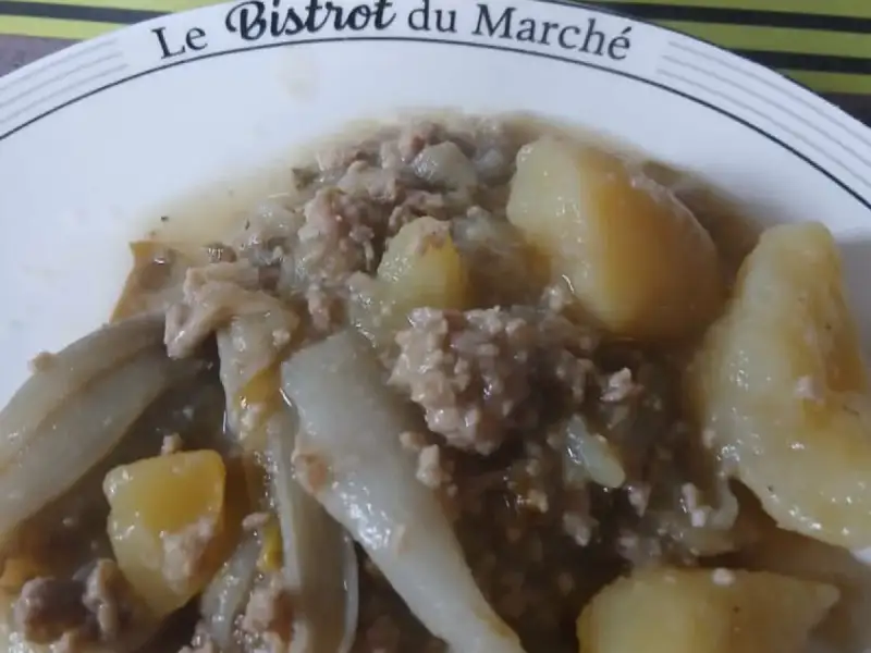 Plato de endivias guisadas con carne molida y papas, con una olla de acero inoxidable al fondo