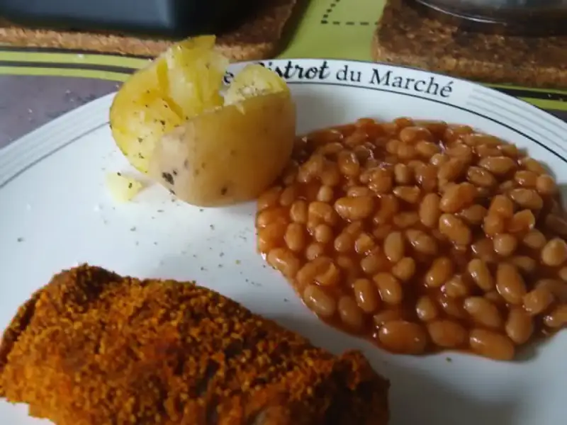 Haché pané croustillant au paprika, haricots blancs à la sauce tomate et pomme de terre en robe des champs sur une assiette