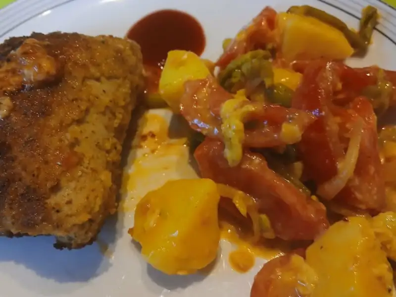 Goldbraune Scheibe Hackbraten mit einer Pfanne Kartoffeln, Tomaten und grünen Bohnen auf einem Teller