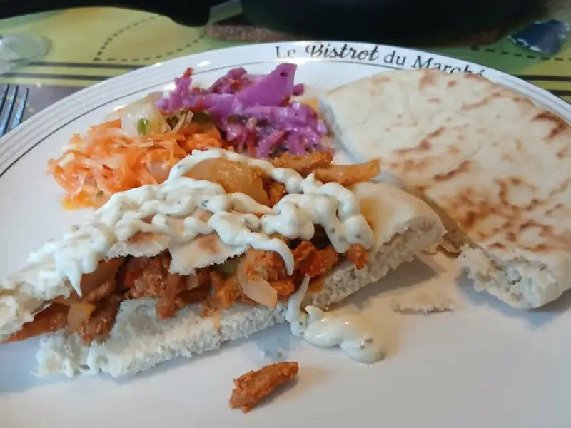 Homemade gyro pita filled with spiced meat and white herb sauce, with red cabbage and grated carrot, skillet in the background