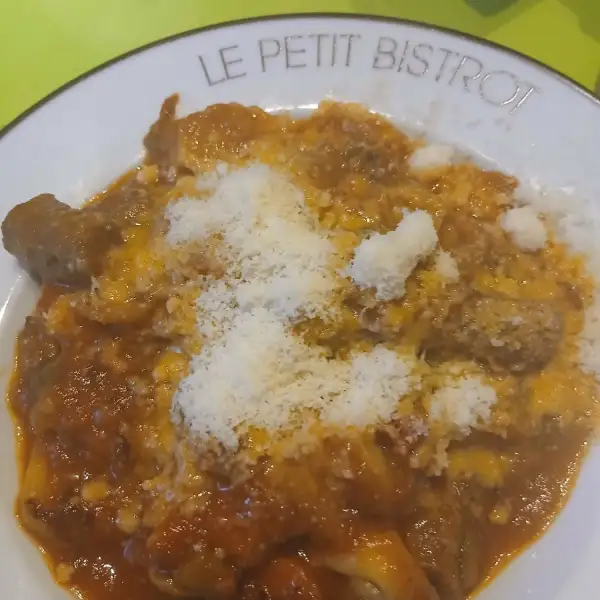 Homemade prosciutto ravioli topped with merguez tomato sauce and grated Parmesan in a shallow bowl