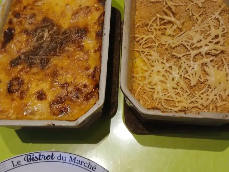 Golden leek gratin and homemade mashed potatoes with a breadcrumb crust, in two baking dishes on a green table