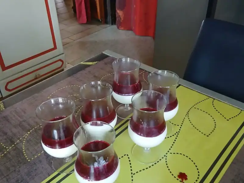 Six verres de panna cotta nappés de coulis de fruits rouges sur une table
