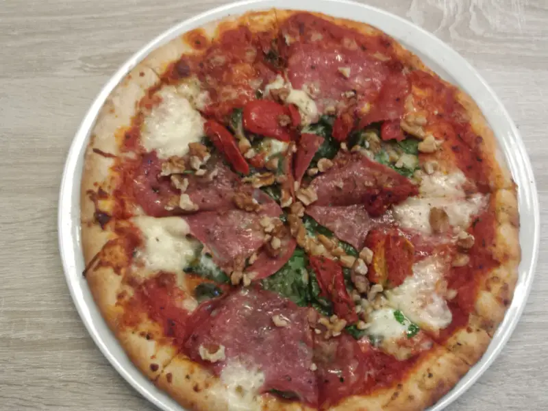 Pizza with salami, vegetables, and grated cheese