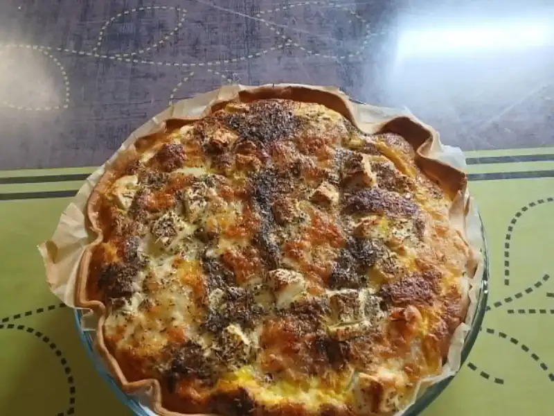Quiche de pollo y queso feta dorada al horno, espolvoreada con hierbas provenzales, en su molde de vidrio