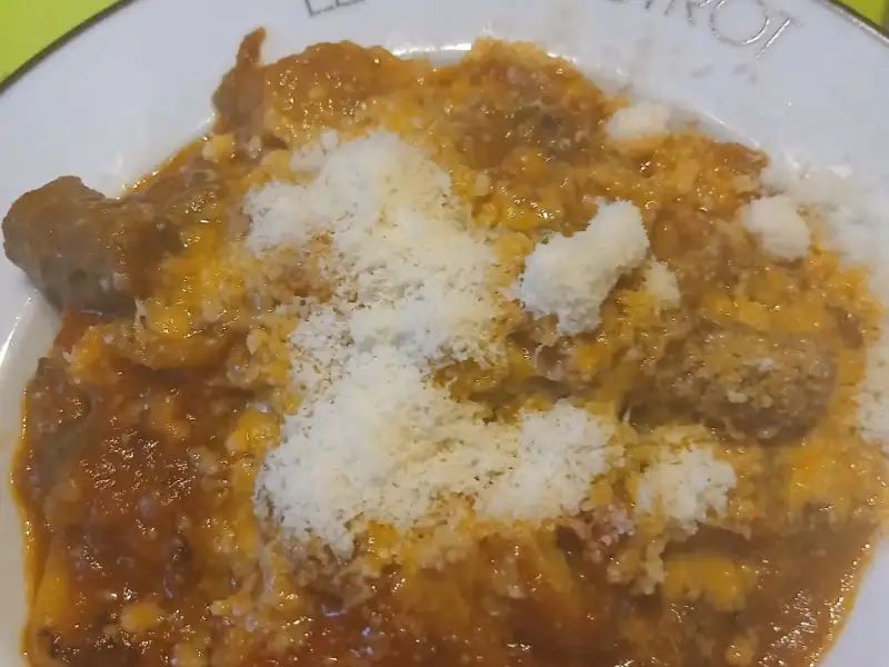 Raviolis maison au jambon de Parme nappés de sauce tomate aux merguez et de parmesan râpé, dans une assiette creuse