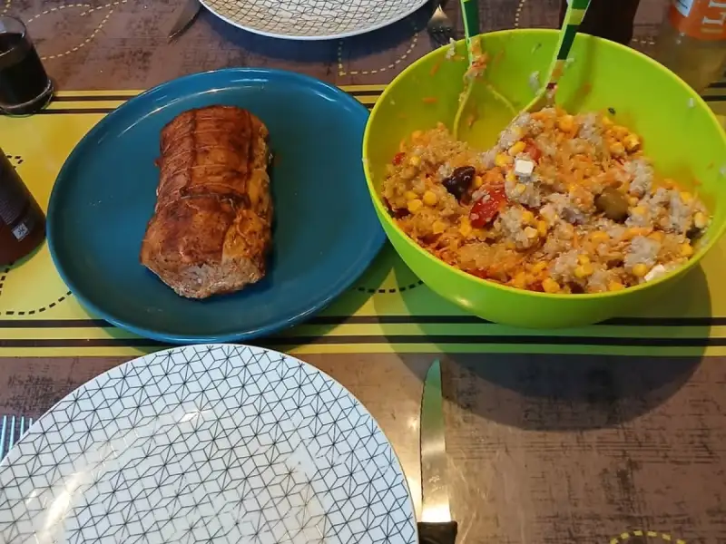 Rôti de saumon doré au four sur une assiette bleue à côté d'un saladier de salade de riz au maïs, tomates, feta et olives