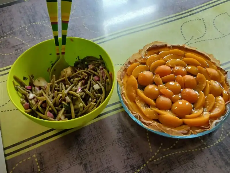 Salade de haricots verts à l'oignon rouge et au concombre dans un saladier vert, à côté d'une tarte aux pêches