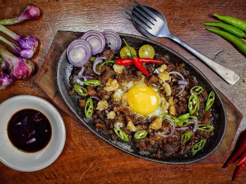 Sisig de cabeça de porco, servido em uma travessa quente.