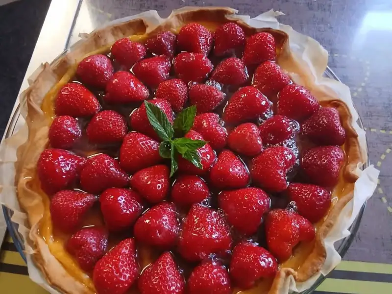 Tarte aux fraises maison nappée, fraises entières sur crème pâtissière, décorée de menthe, dans un moule en verre
