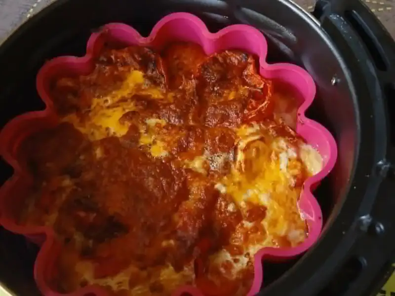 Gegratineerde tomatenclafoutis met kaas in een roze siliconen vorm, in de mand van een airfryer